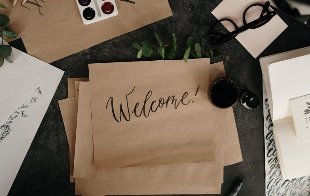 A creative workspace featuring calligraphy, envelopes, and art supplies for crafting personalized welcome cards.